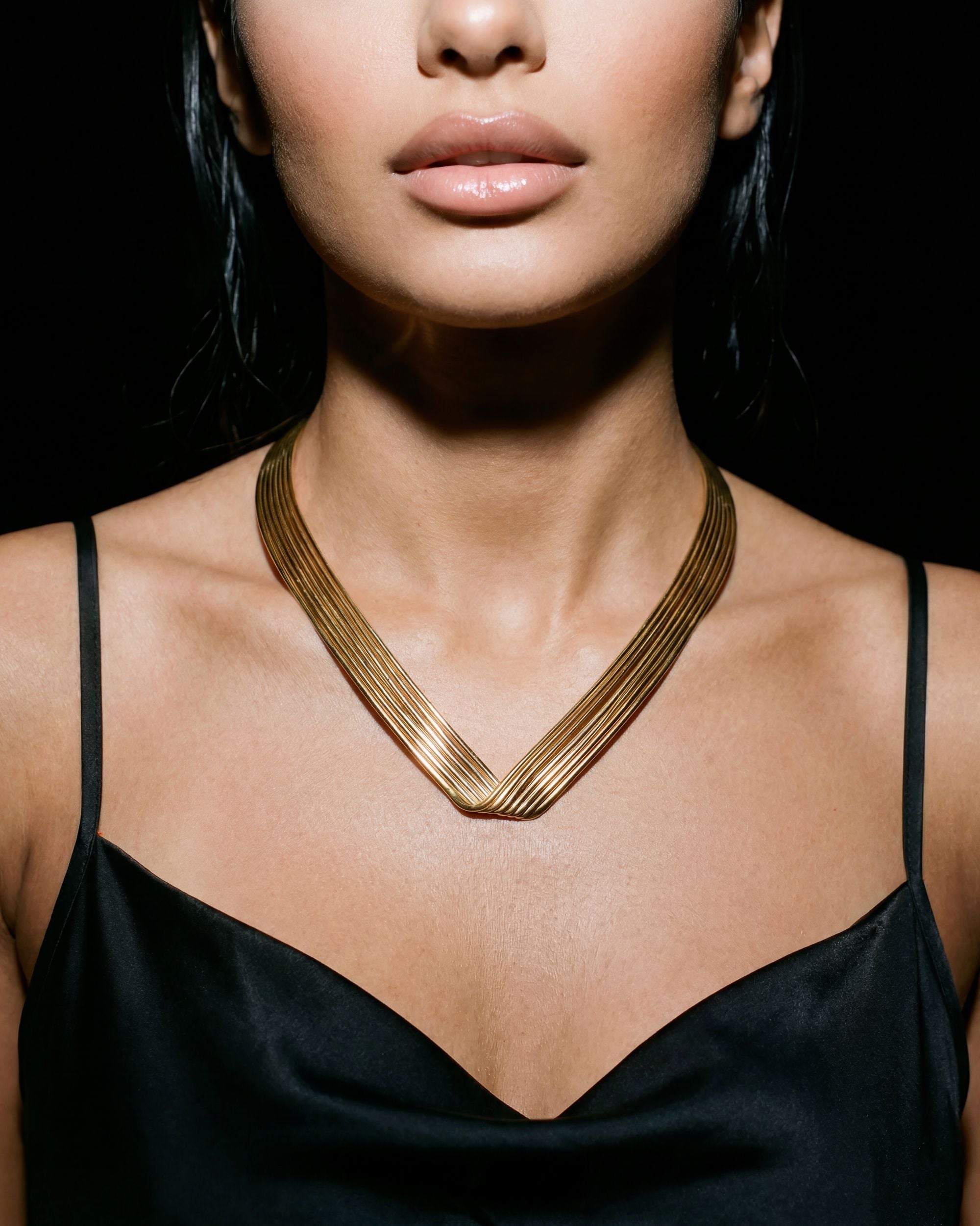 Woman wearing a gold necklace against a black background