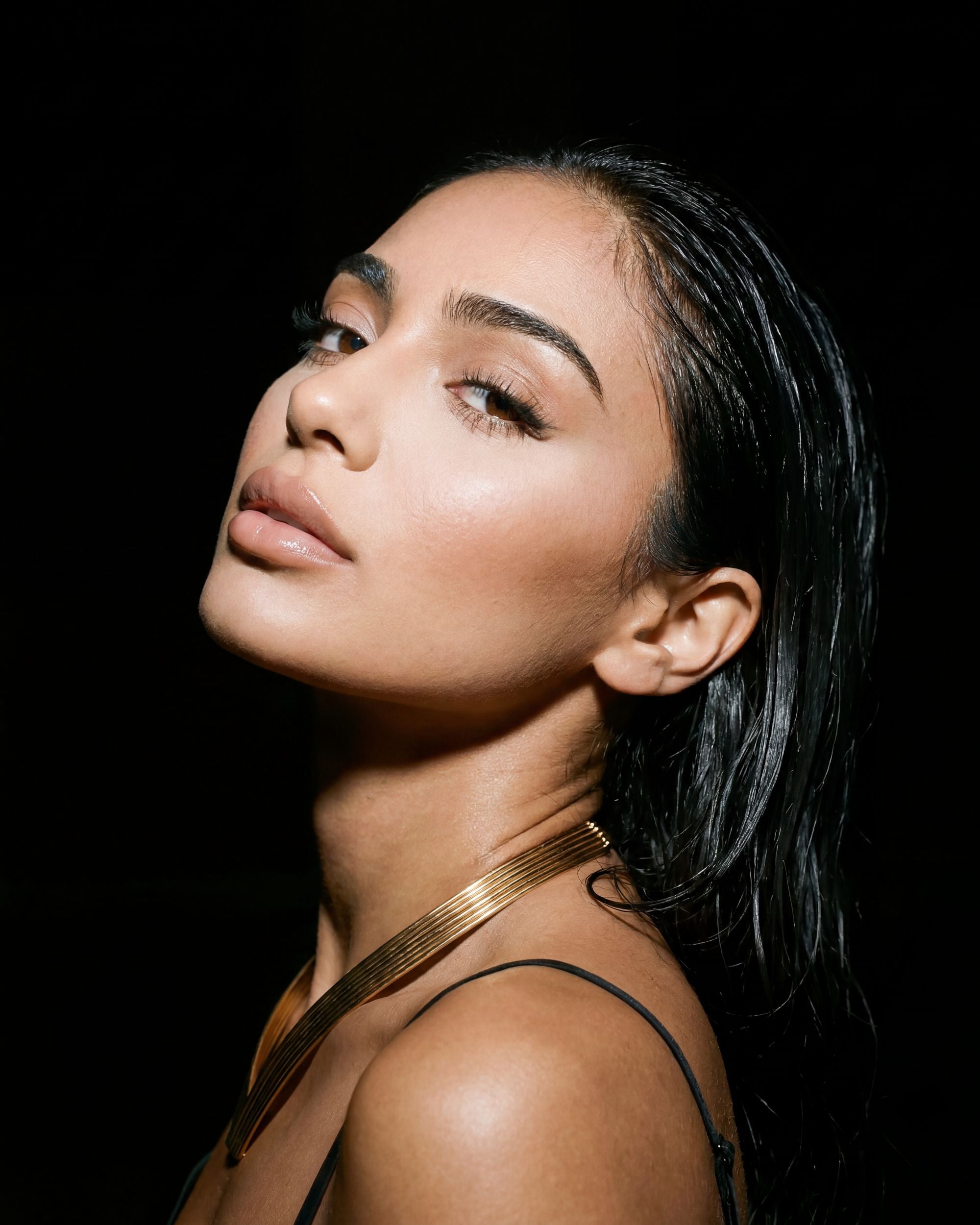 Woman wearing a gold necklace against a black background