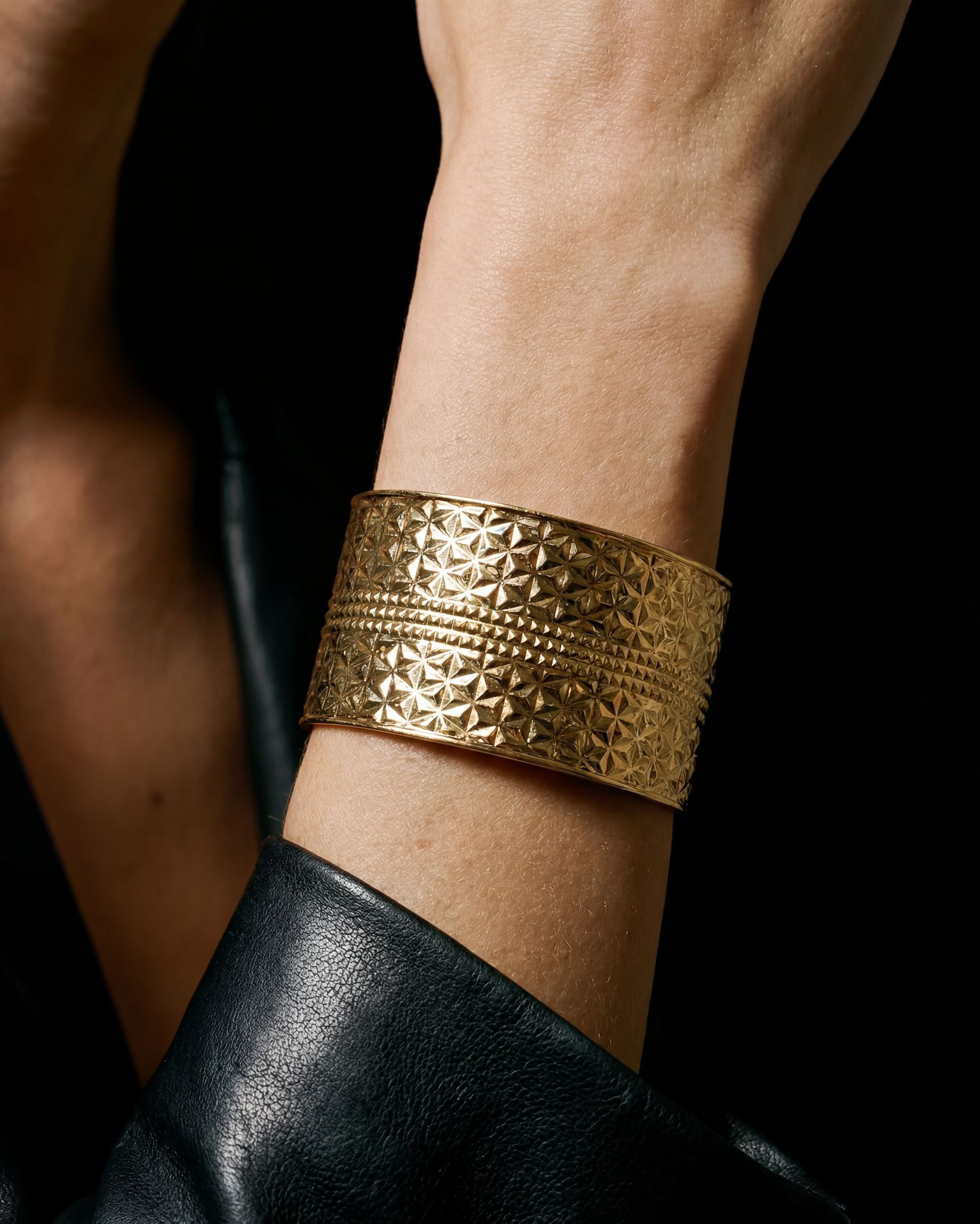 Gold bracelet with geometric pattern on a wrist against a black background