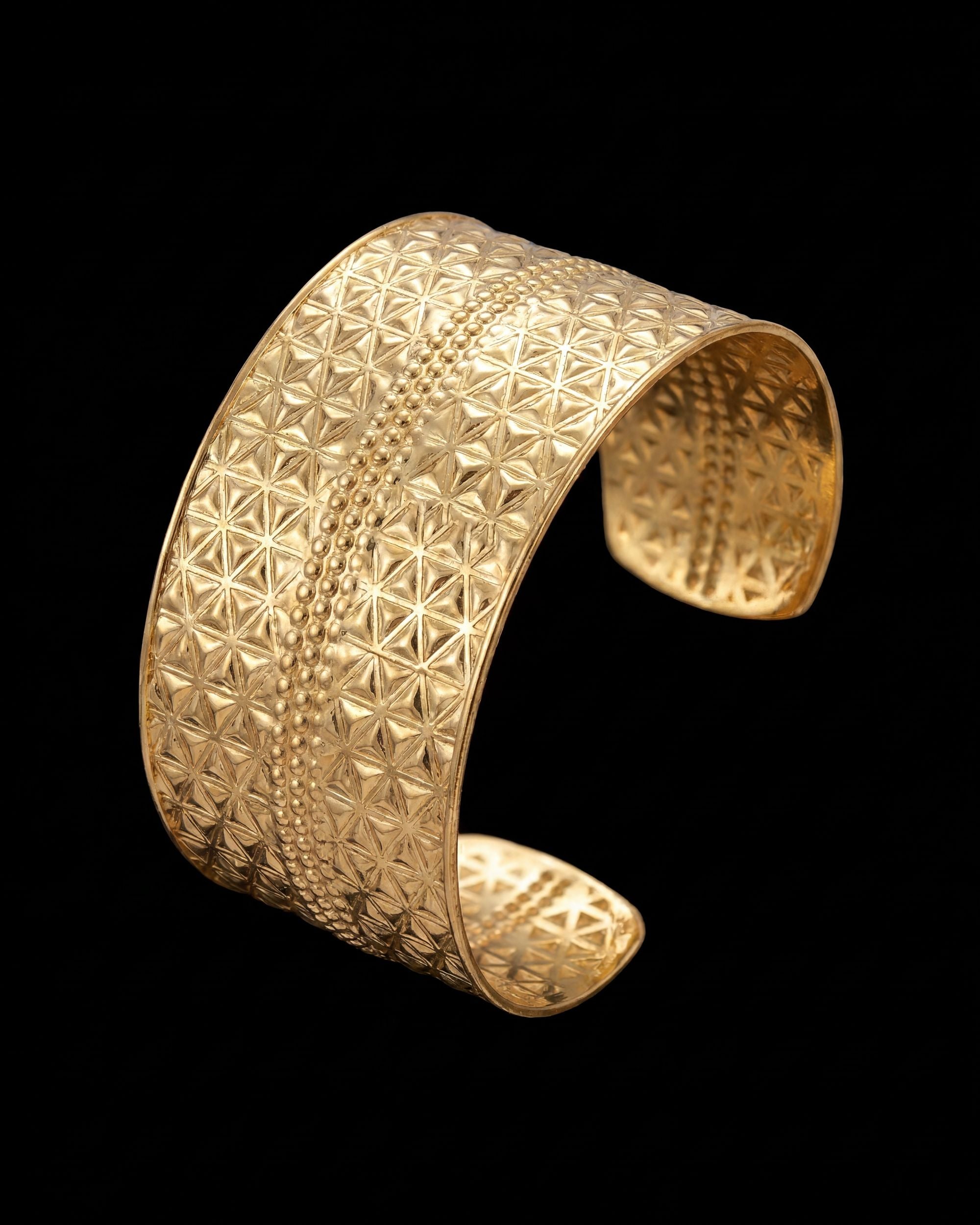 Gold cuff bracelet with intricate pattern on a black background