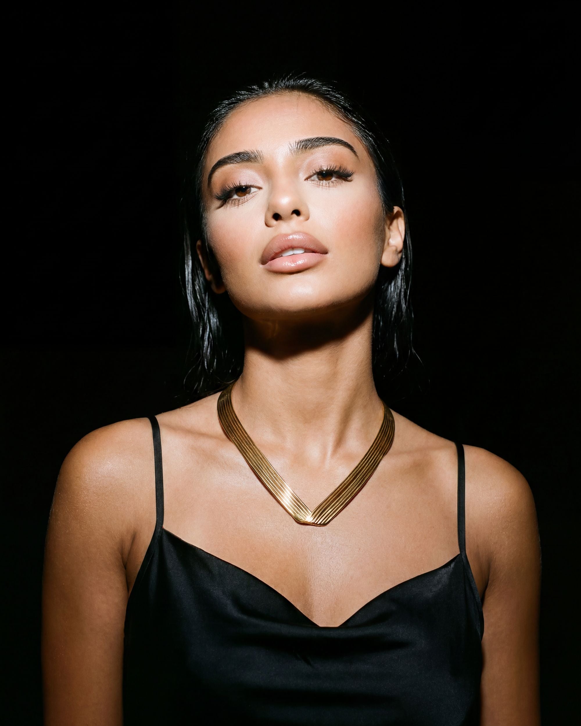 Woman wearing a black dress and gold necklace against a black background
