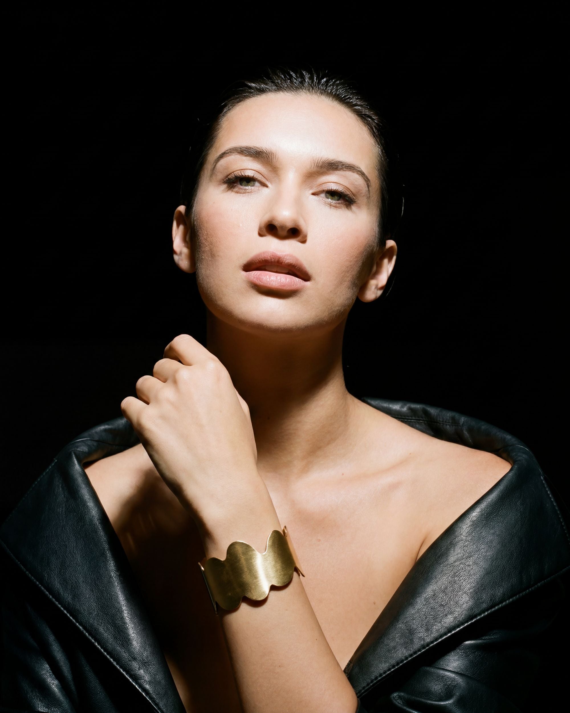 Woman wearing a gold bracelet on a black background