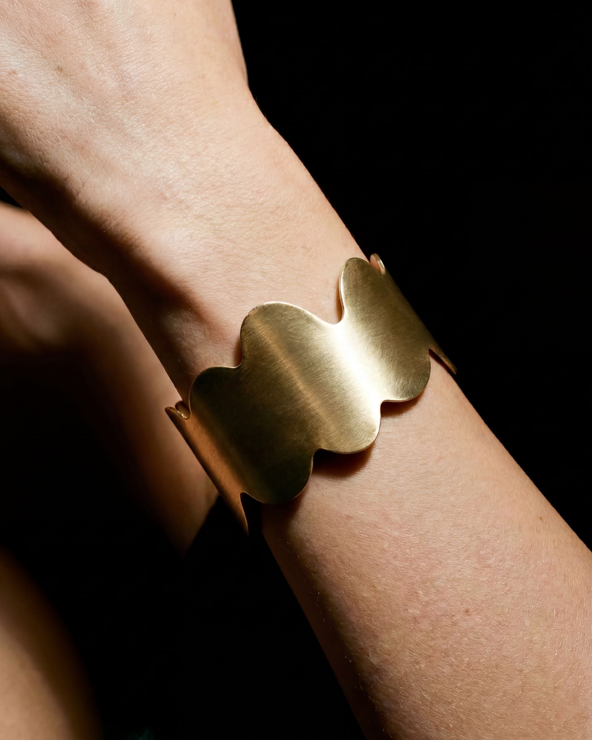 Gold bracelet on a wrist against a dark background